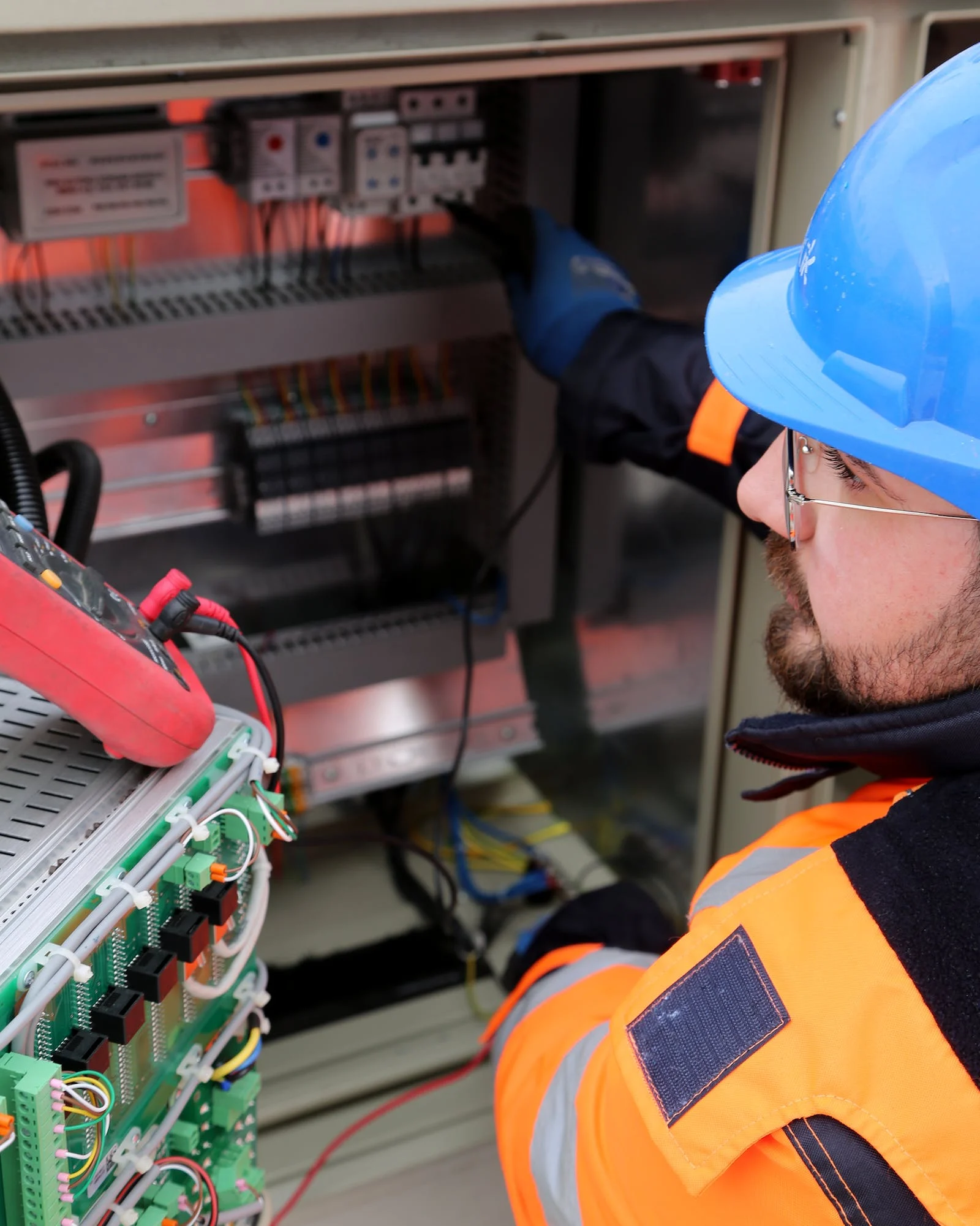 Électricien réparant un tableau de disjoncteurs tout en regardant le multimètre